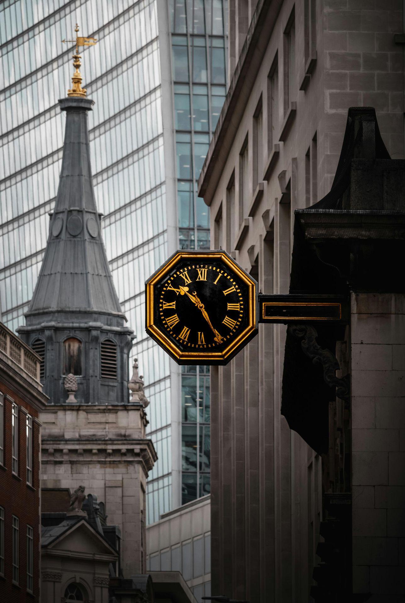 Street view of a vintage clock on a building with modern and classic architecture in the background.