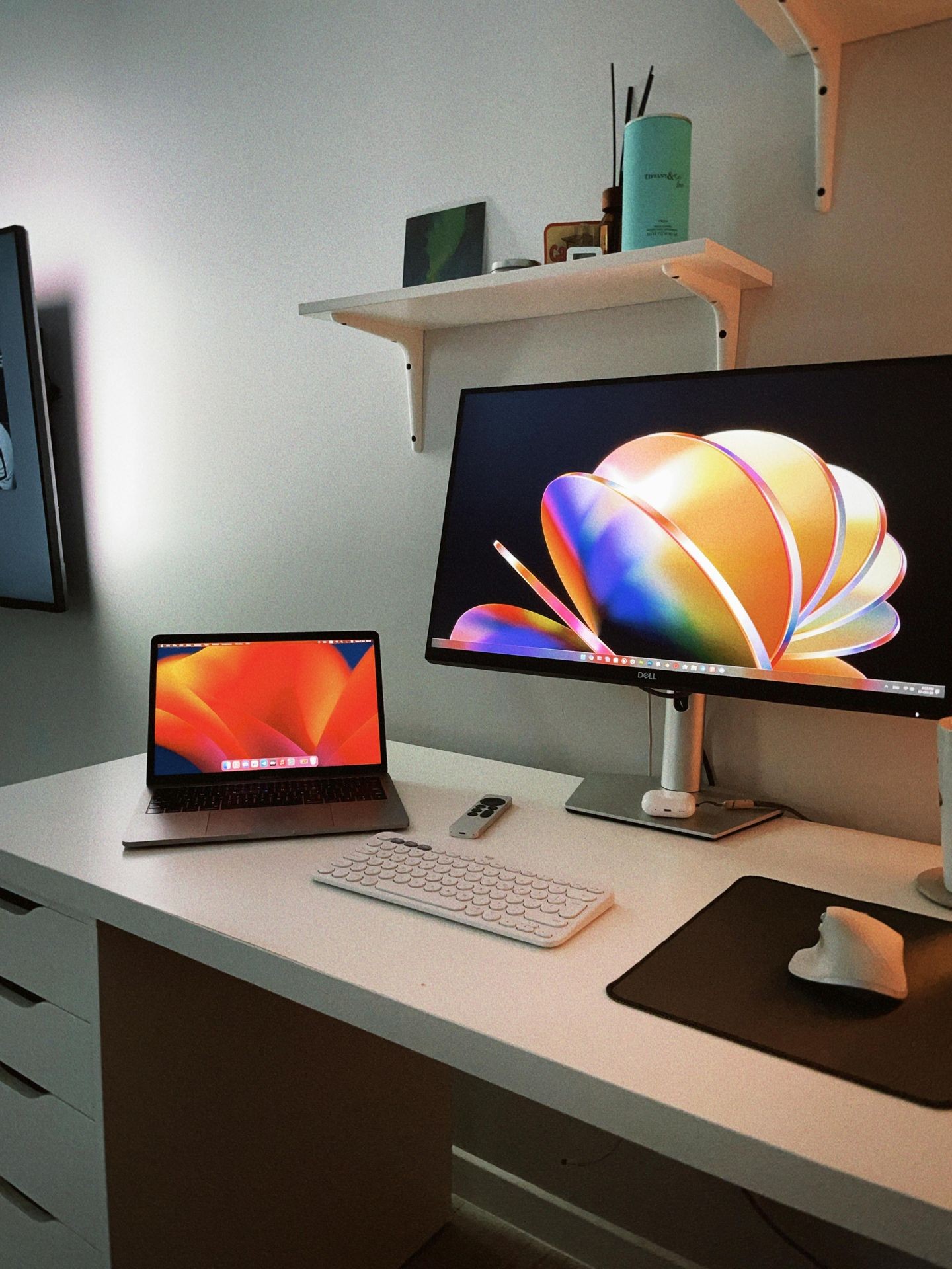 Minimalist desk setup with laptop and monitor displaying colorful abstract images, wireless keyboard and mouse.